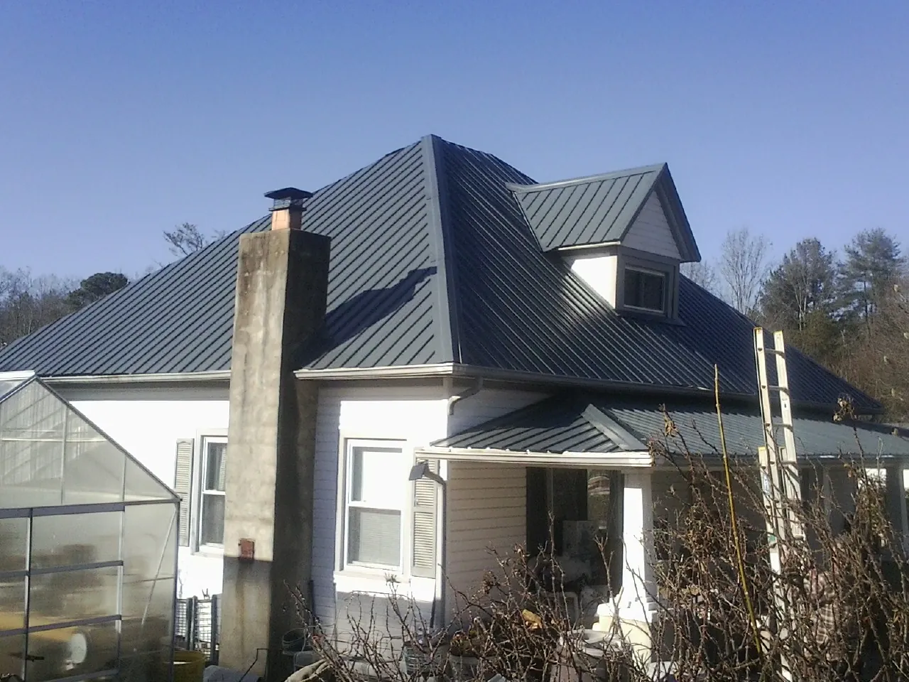 Dark blue standing seam metal roof on a white farmhouse with dormer — Slate & Tile Roof Repair by Roofing Brothers in Turin