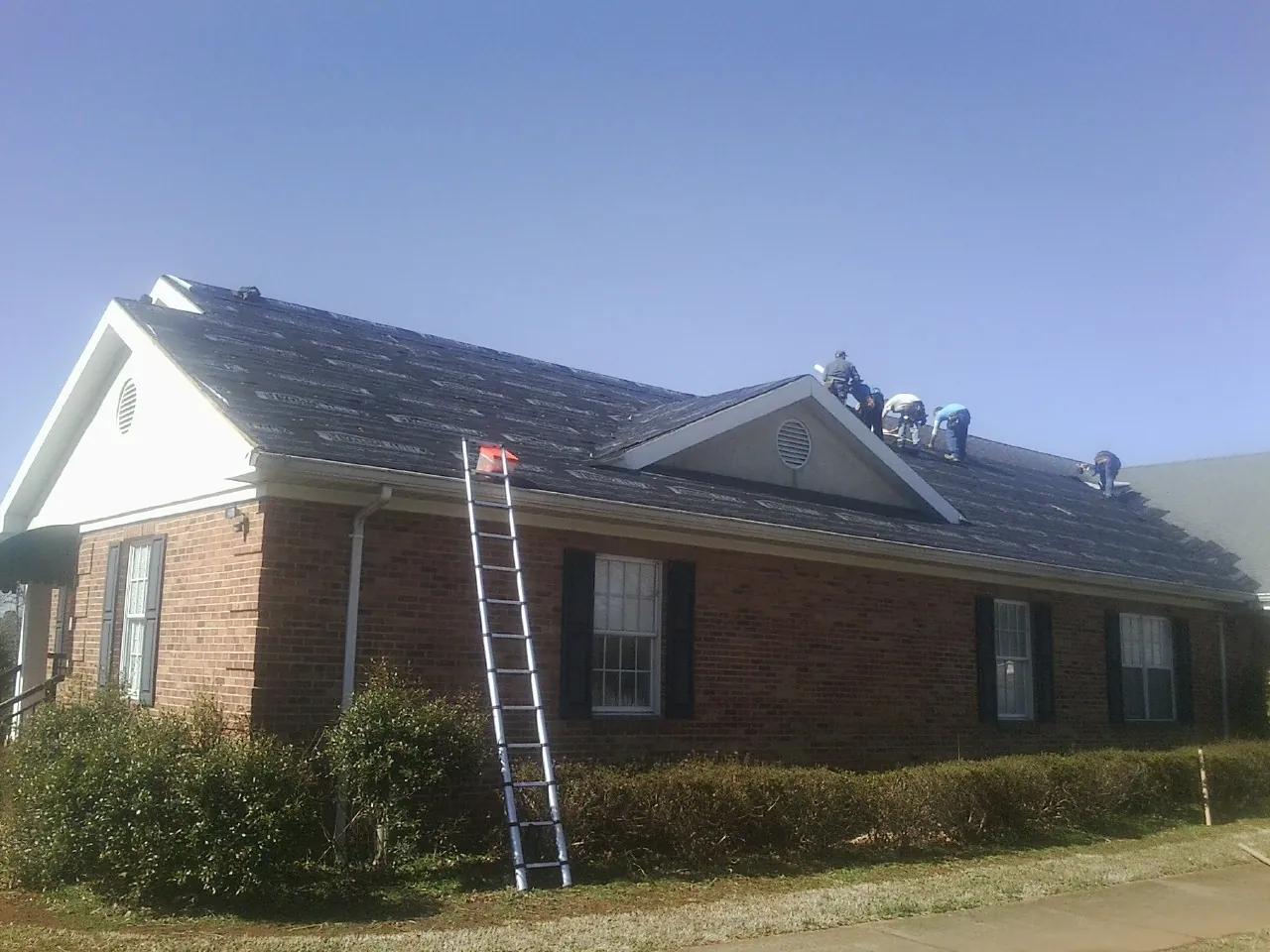 Crew tearing shingles off a brick ranch roof with a ladder set — Metal Roof Repair work by our crew in Turin