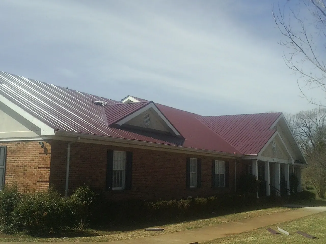 Red metal roof with gabled entries on a long brick building, from a Hail Damage Roof Repair job in Turin