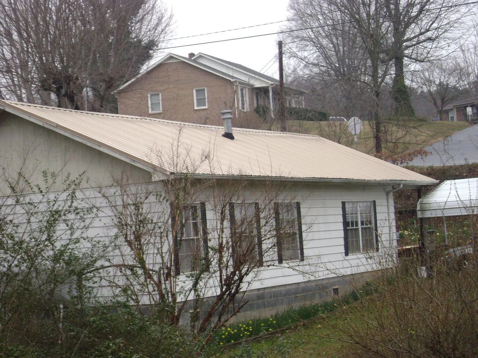 Tan metal roof on a white sided house set into a hillside — Commercial Roofing by Roofing Brothers in Turin