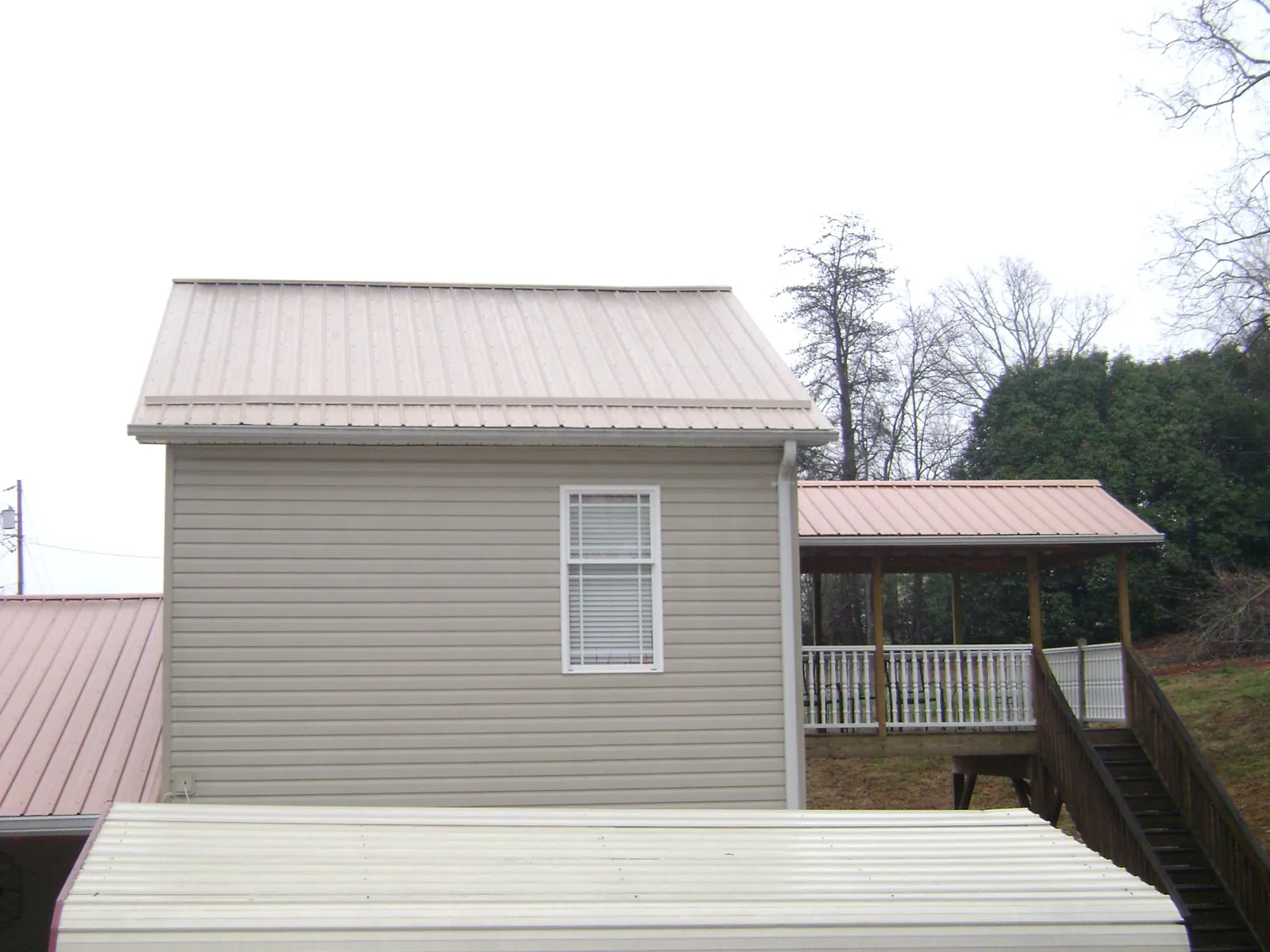 Tan metal roofs on a two story addition and attached porch, from a Roof Replacement job in Turin